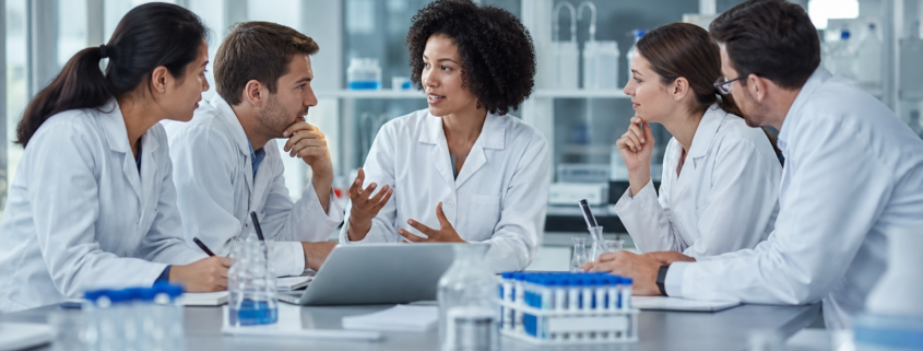 diverse scientists in lab coats collaborating at a lab table, showing biotech team building.
