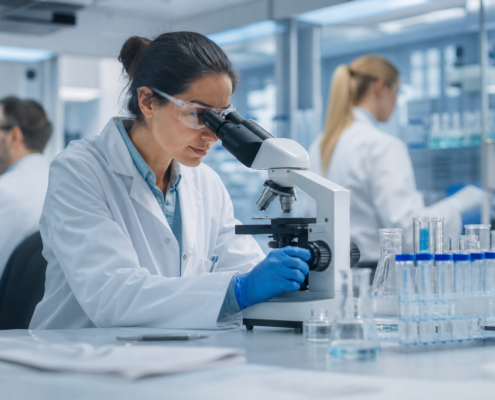 female scientist in safety glasses examining samples under a microscope in a lab to attract experienced biotech researchers.