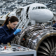 female technician in safety glasses working on a complex jet engine, highlighting aerospace manufacturing jobs.