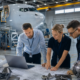 three engineers reviewing blueprints and laptop in an aircraft hangar, for aerospace recruitment september.