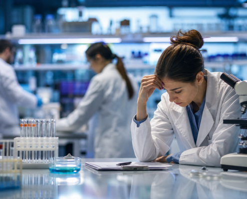 stressed female biotechnology researcher with a microscope, illustrating challenges in biotechnology researcher retention.