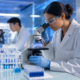 female scientist in lab coat and gloves examining samples with a microscope for life sciences contract staffing.