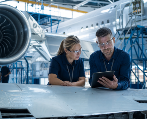 two engineers reviewing a tablet on an airplane wing, showing aerospace manufacturing jobs october operations.