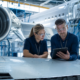two engineers reviewing a tablet on an airplane wing, showing aerospace manufacturing jobs october operations.